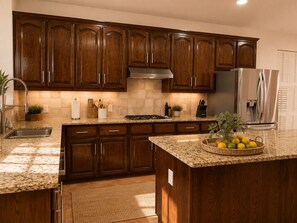 A kitchen with wooden cabinets, a stainless steel refrigerator, granite countertops, and a center island with a fruit bowl.