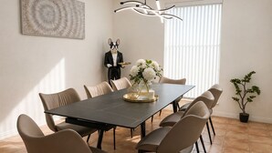 Un comedor con una mesa larga, seis sillas, una estatua decorativa, un florero con flores y una planta en maceta.