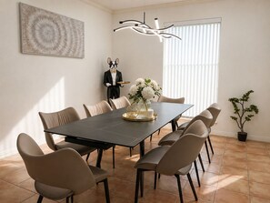 A dining area with a long table, six chairs, a decorative statue, a vase with flowers, and a potted plant.