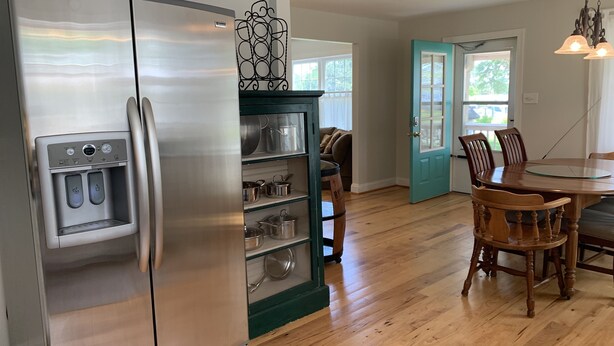 A kitchen with a stainless steel refrigerator, a built-in oven, and a water dispenser. There is a wooden dining table with chairs and a teal door leading to another room. - Coffee Creek Cottage: A tranquil, waterfront escape minutes from Oriental, NC (Merritt)