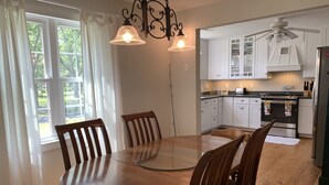 A dining area with a wooden table and chairs, a kitchen with white cabinets, and a ceiling fan. - Coffee Creek Cottage: A tranquil, waterfront escape minutes from Oriental, NC (Merritt)