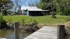 A wooden dock leading to a house with a metal roof, surrounded by greenery and trees. - Coffee Creek Cottage: A tranquil, waterfront escape minutes from Oriental, NC (Merritt)