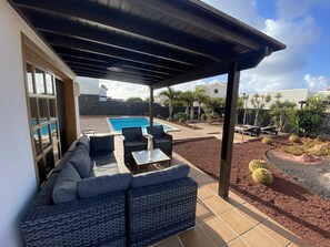 An outdoor patio area with a pool, a covered seating area with sofas and chairs, and a landscaped garden with cacti and shrubs. - Luxury villa with private heated pool (PLAYA BLANCA)