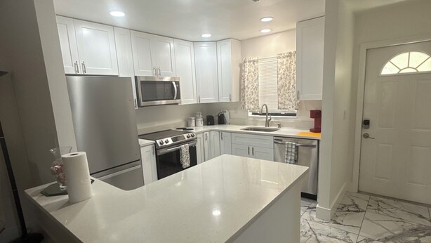 A modern kitchen with white cabinets, a stainless steel refrigerator, a microwave, and a sink. - 2/2 Duplex on CANAL all updated; new furniture, (Rotonda West)