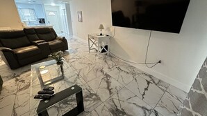 A modern living room with a large flat-screen TV mounted on the wall, a leather sofa, a glass coffee table, and a marble-patterned floor. - 2/2 Duplex on CANAL all updated; new furniture, (Rotonda West)