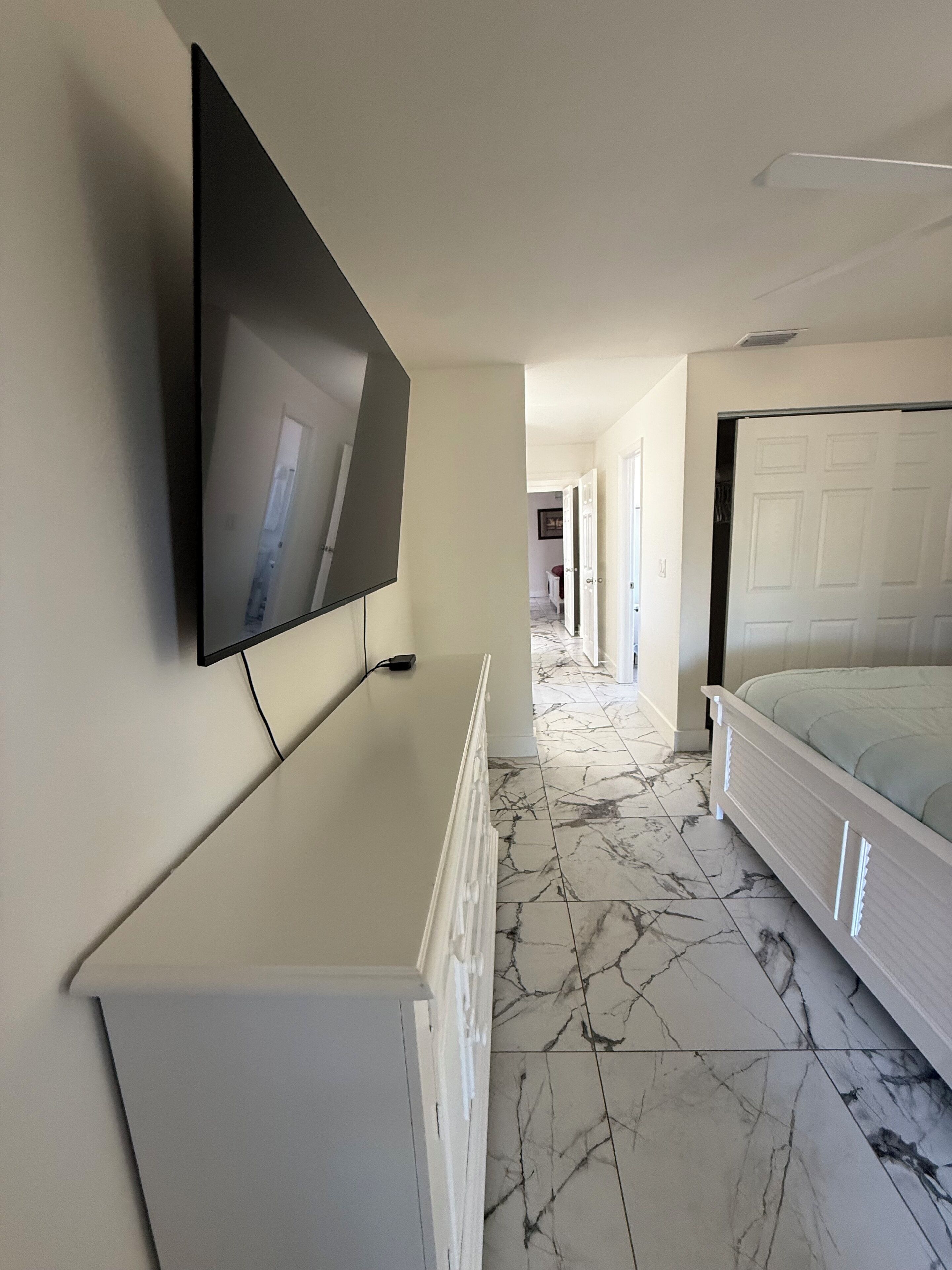 Une chambre à coucher avec un lit, un téléviseur fixé au mur et un sol à motifs de marbre.