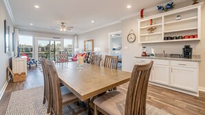 A spacious dining area with a wooden table and chairs, a kitchen with white cabinets and a coffee station, and a view through the glass doors. - The Lookout - Lake Views, Swim, Fish, & More! (Hot Springs)