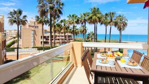 Ein Balkon mit Frühstückstisch, der Blick auf einen Strand mit Palmen und einen klaren Himmel bietet.