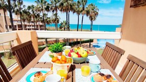 Ein Tisch mit Frühstücksangeboten, einer Obstschale und Blick auf Strand und Palmen.
