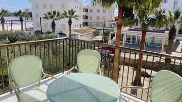 Een balkon met twee stoelen en een tafel, uitkijkend op een straat met gebouwen en palmbomen.