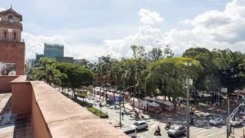 A busy urban street with a prominent clock tower, greenery, and modern buildings.