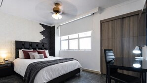 A modern bedroom with a black headboard, a bed with white and red bedding, a desk with a chair, and a large window. - Luxury Apartment! Amazing location! Poblado! Lleras! Provenza! Air Conditioning! (Antioquia)