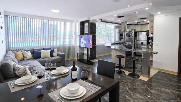 A modern living room with a sofa, dining table set for a meal, and a kitchen area with a TV. - Luxury Apartment! Amazing location! Poblado! Lleras! Provenza! Air Conditioning! (Antioquia)