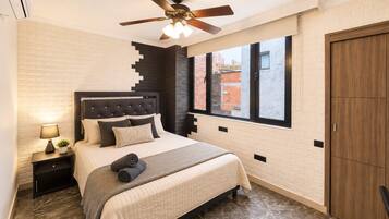 Quarto com cama, mesas de cabeceira, ventoinha no teto, janela e guarda-roupa.