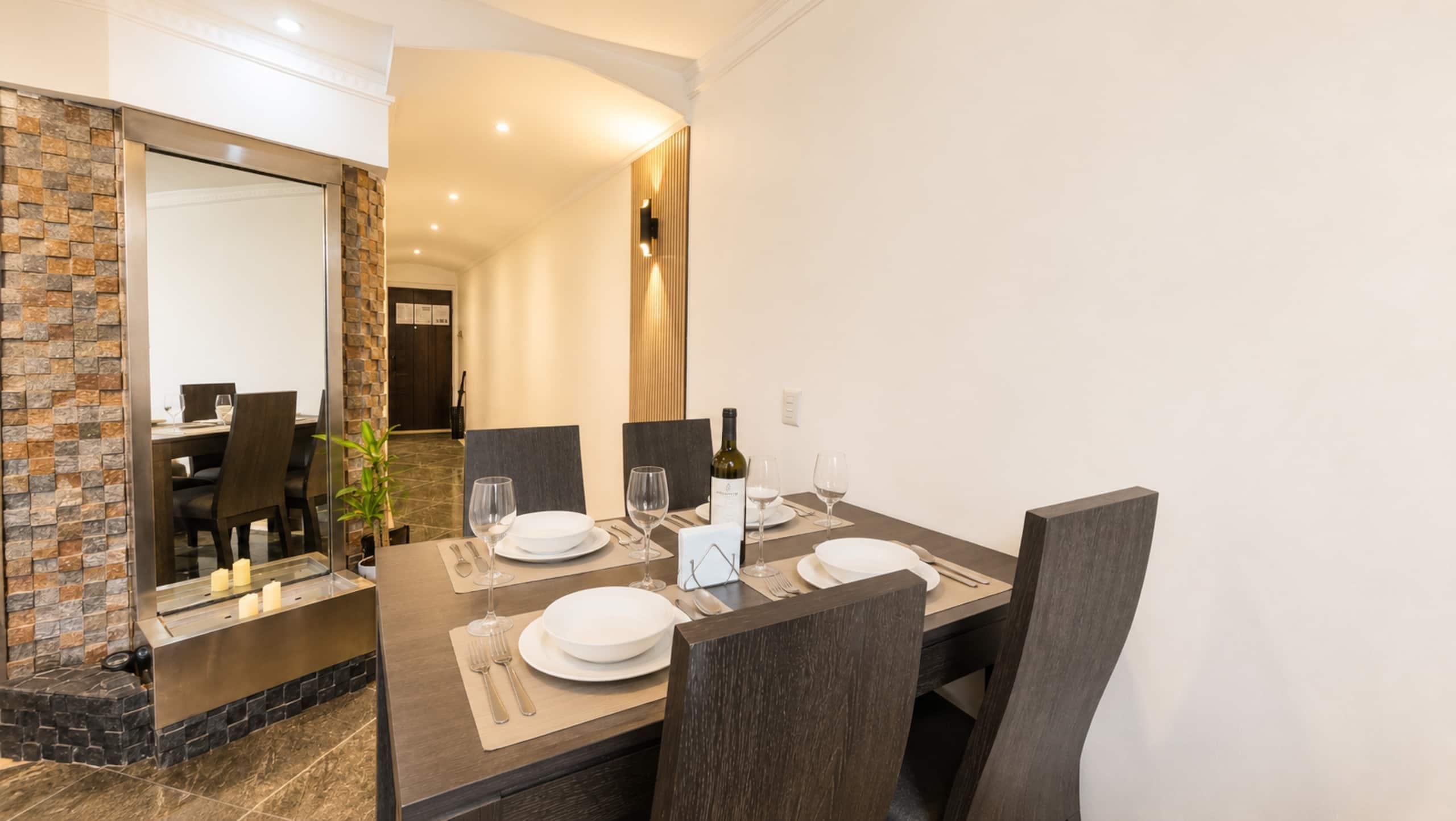 A modern dining area with a dark wooden table set for four, including plates, glasses, and cutlery.