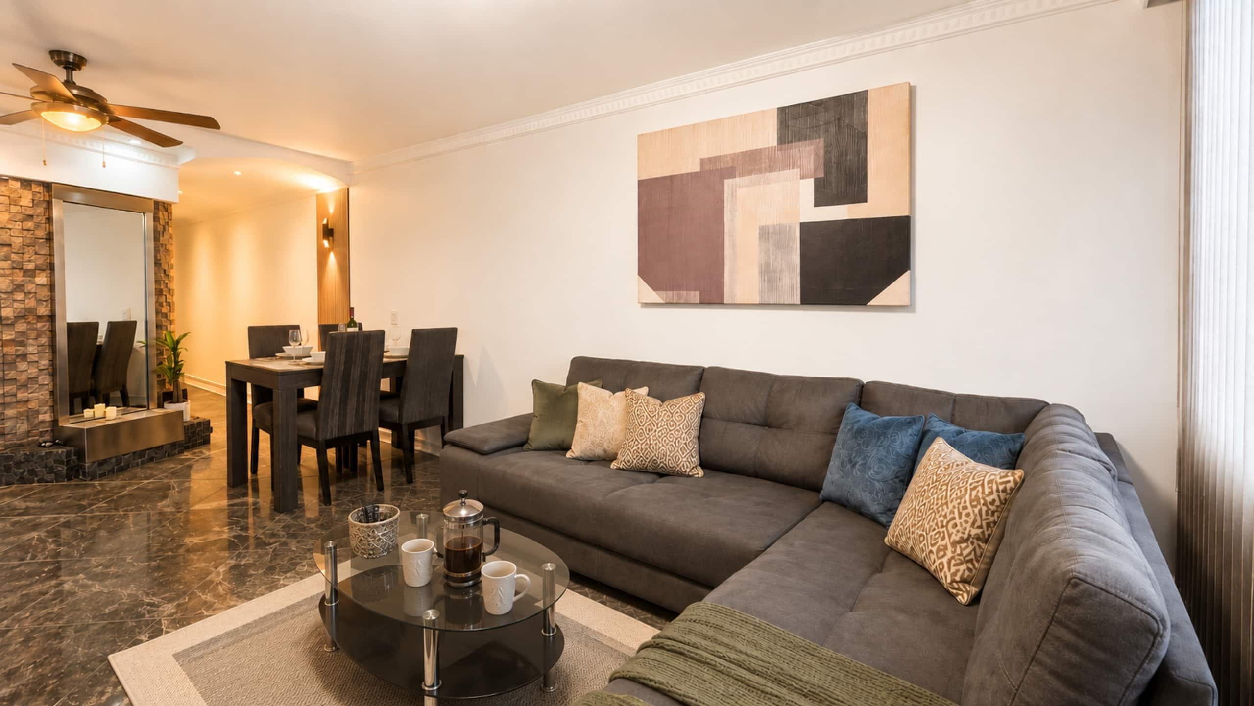 Uma sala de estar moderna com um sofá seccional, uma mesa de centro e um espaço de jantar com cadeiras e uma mesa.