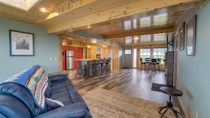 A spacious living room with a large sofa, a kitchen area with wooden cabinets, a dining table with chairs, and a bar area. - Sand Ranch - Epic Ocean View and SPA (Gold Beach)