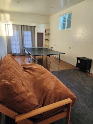 A room with a ping pong table, a sofa, a small table, and a window. - Sand Ranch - Epic Ocean View & Spa (Gold Beach)