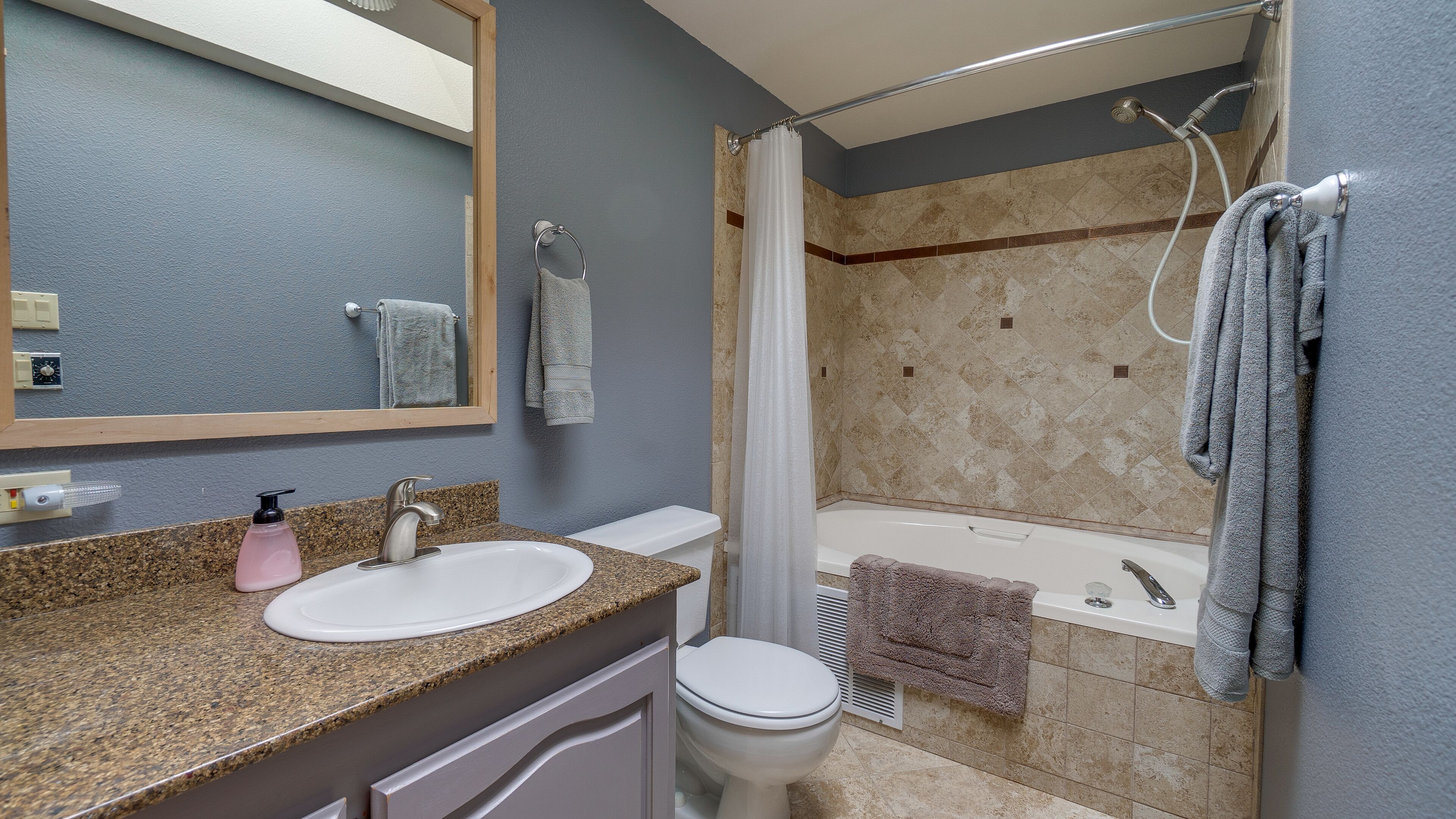 Une salle de bain avec un comptoir en granit, un lavabo blanc, des toilettes, une douche avec une porte en verre et une baignoire.