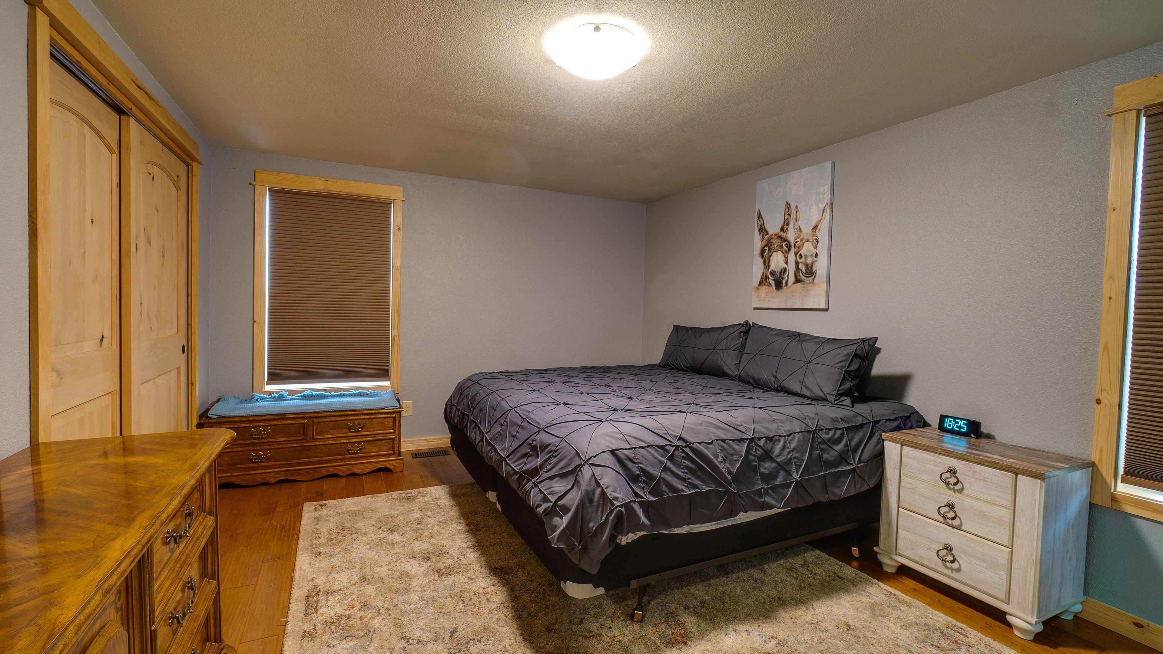 Een slaapkamer met een bed, een dressoir, nachtkastje en een raam met jaloezieën.