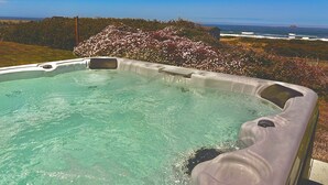 A hot tub with a clear view of the ocean and a garden with blooming flowers. - Sand Ranch - Epic Ocean View and SPA (Gold Beach)