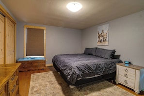 Un dormitorio con cama, mesita de noche, cómoda, ventana con persianas y un reloj de pared.