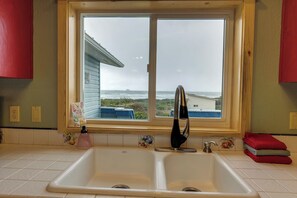 A kitchen with a double sink, a window with a view of the sea, and a red towel on the counter. - Sand Ranch - Epic Ocean View & Spa (Gold Beach)