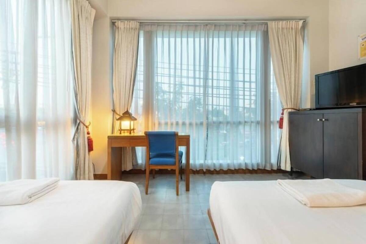 A hotel room with two beds, a desk, a chair, a television, and a window with curtains.