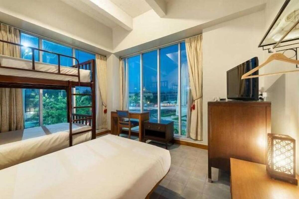A hotel room with bunk beds, a desk, a television, and large windows offering a city view.