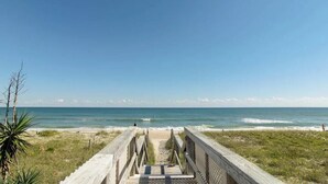 Ein hölzerner Steg führt zu einem Strand unter blauem Himmel.
