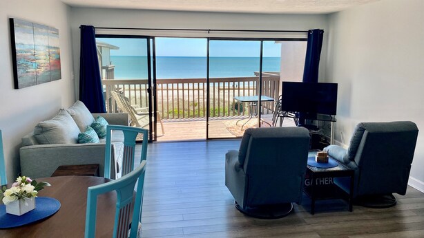 Ein Zimmer mit Balkon und Meerblick, eine Couch, zwei Sessel, ein Tisch und ein Fernseher.