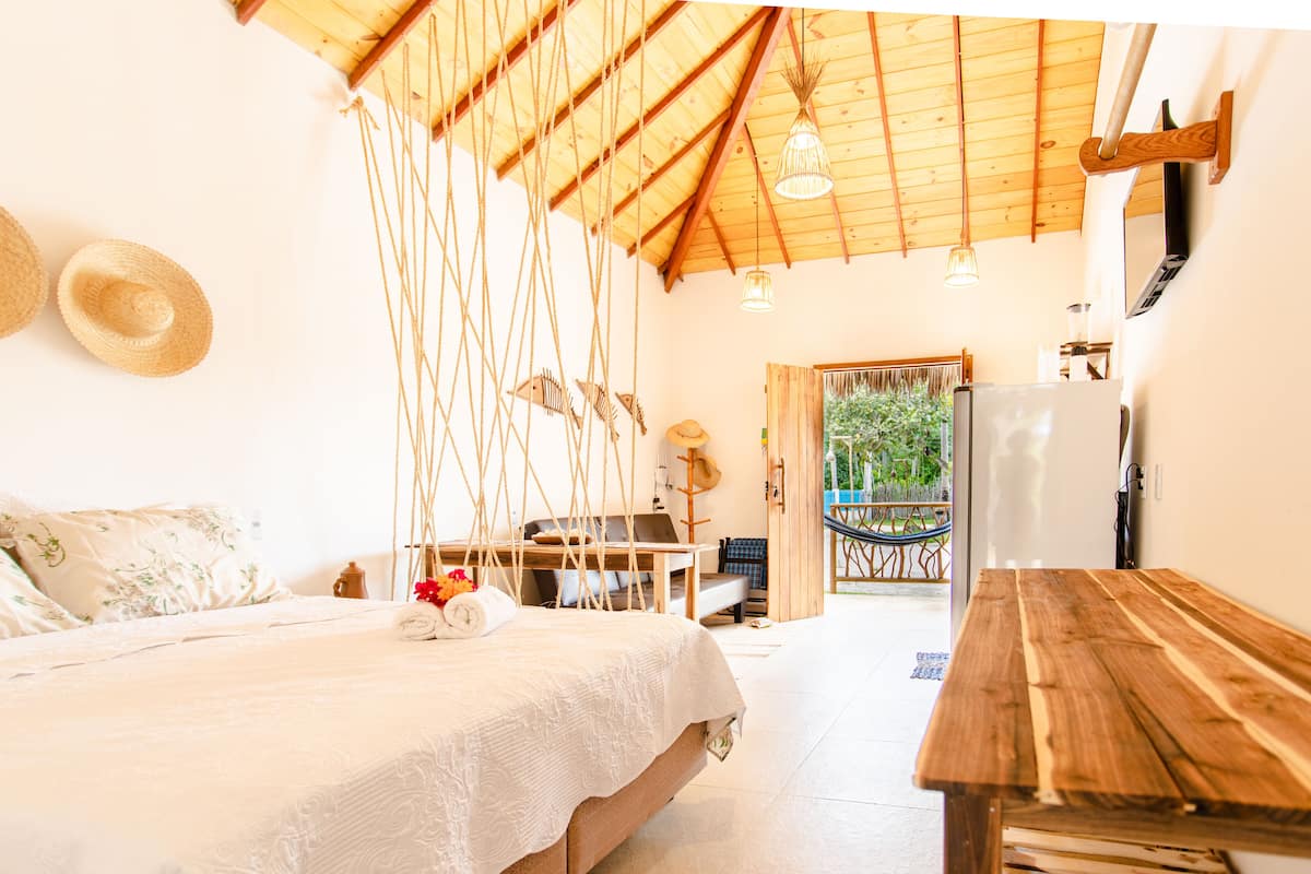 A cozy room with a bed, a wooden table, a desk, and a hammock.