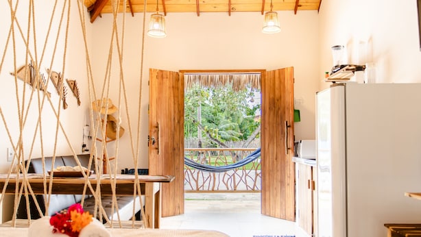 Een kamer met een bed, een bureau, een hangmat en uitzicht op de omgeving.