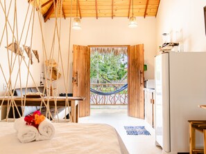 Une chambre avec un lit, un bureau, un hamac et une vue sur l’extérieur.