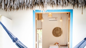 Een hangmat op een balkon met uitzicht op een kamer, daarin een bed, een tafel en een hanglamp.