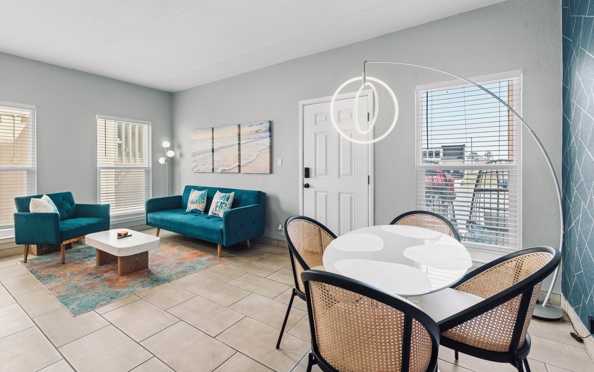 A living room with a teal sofa, white coffee table, wicker chairs, and artwork on the wall.