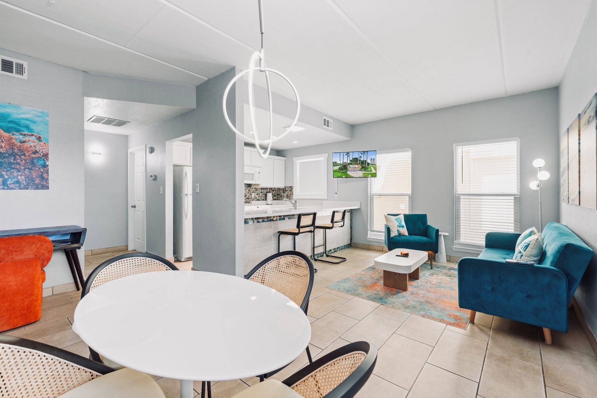 A modern living room with a round dining table, a sofa, and a kitchen area with a TV.