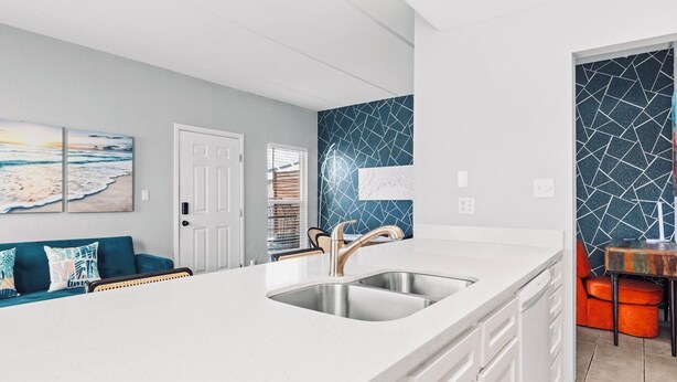 A modern kitchen with a white countertop, stainless steel sink, and a blue-tiled backsplash.