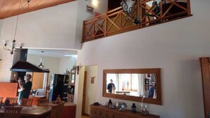 Un espace repas avec des meubles en bois, un plafond haut et un grand miroir placé au-dessus d’une commode en bois.