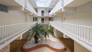 Ein mehrgeschossiges Atrium mit einem zentralen Garten, weißen Geländern und Blick auf einen klaren Himmel.