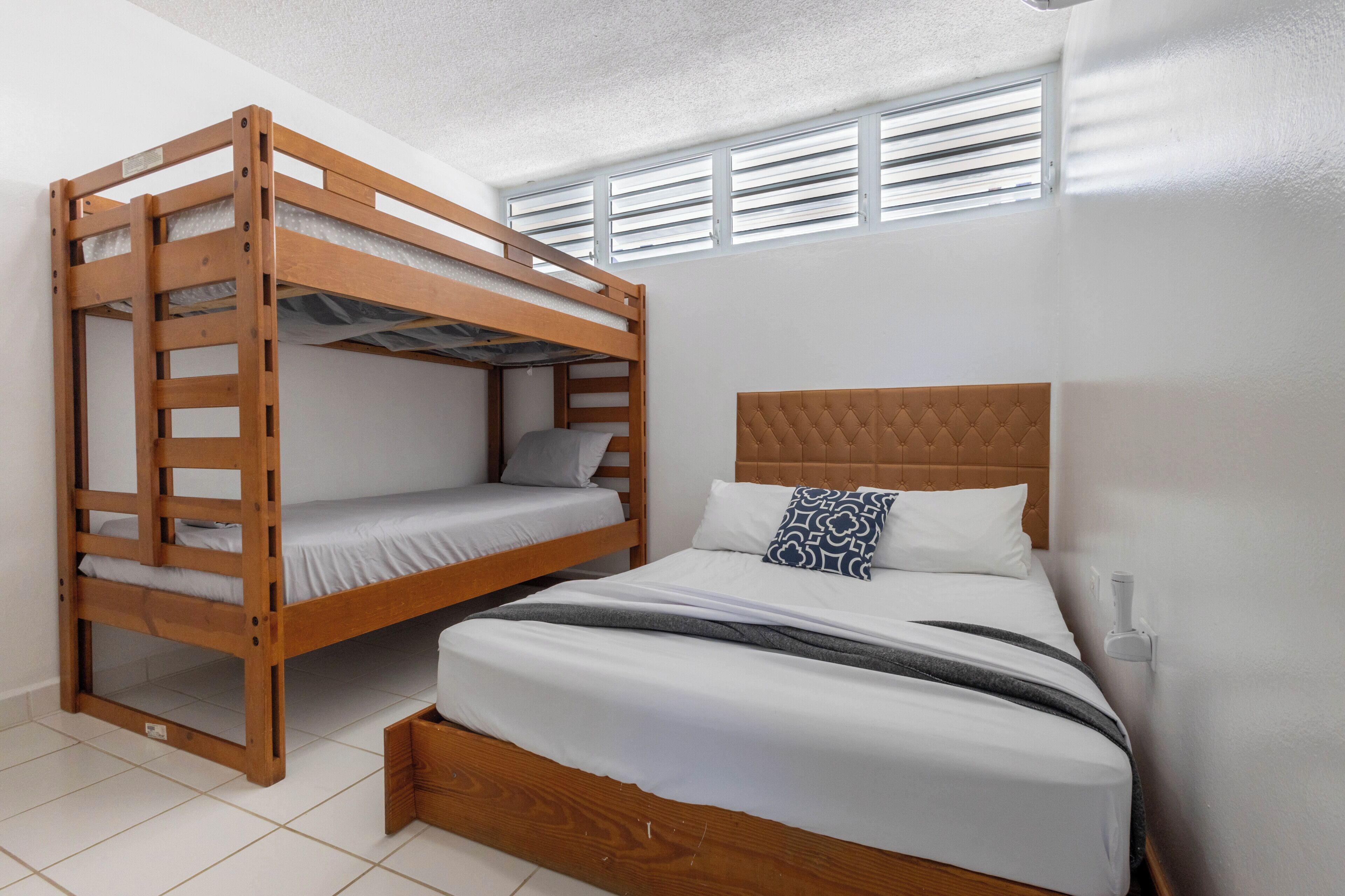 Un lit superposé avec une structure en bois, un lit simple en bas et une tête de lit à motifs capitonnés.