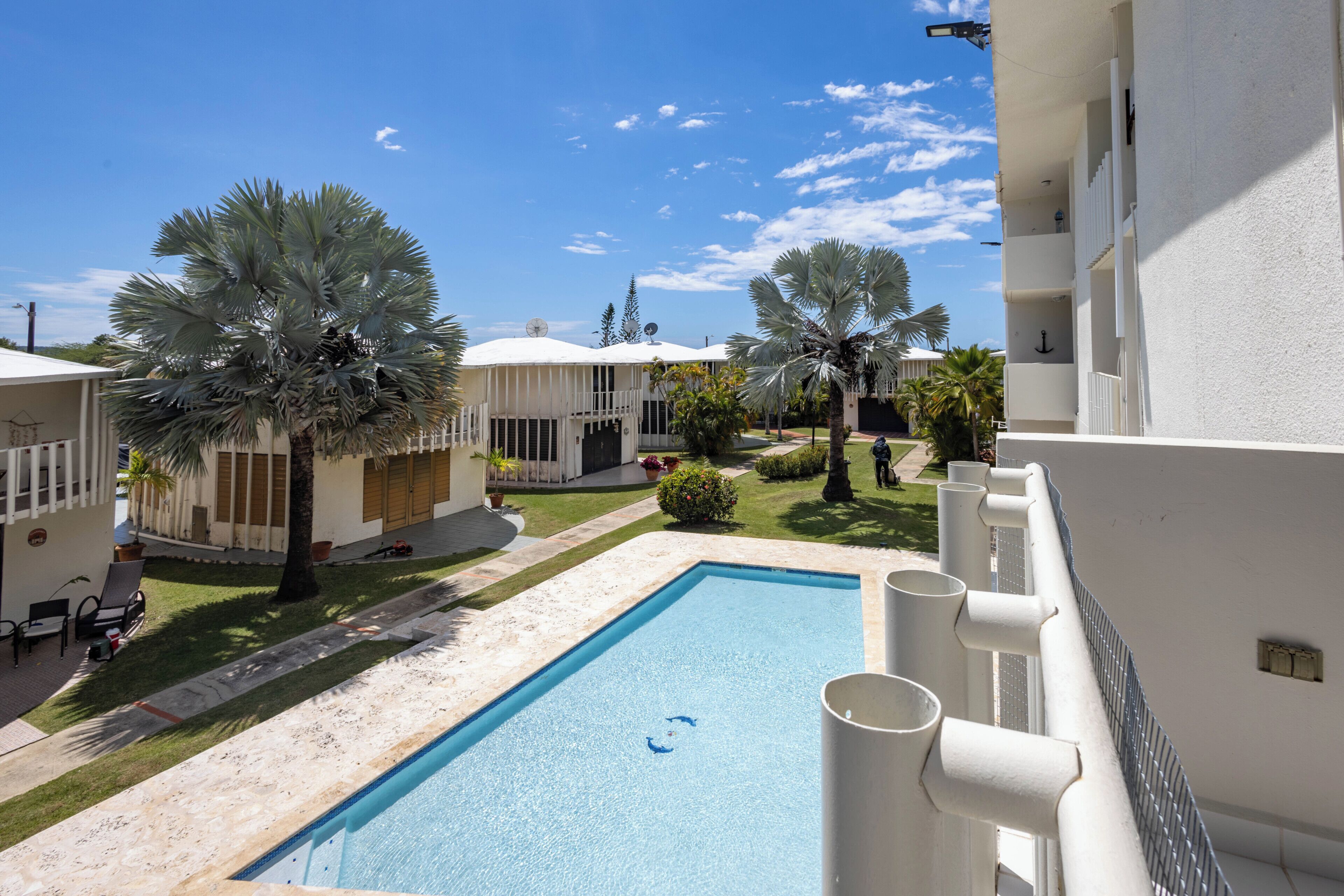 A pool with a clear blue sky, palm trees, and a white building with balconies.