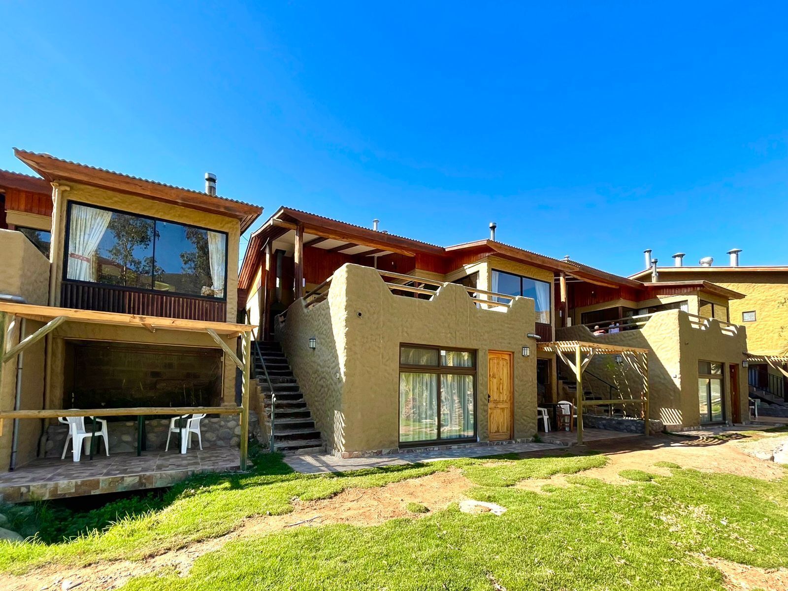 A modern building with multiple balconies, a covered outdoor seating area, and a staircase leading to an upper level.