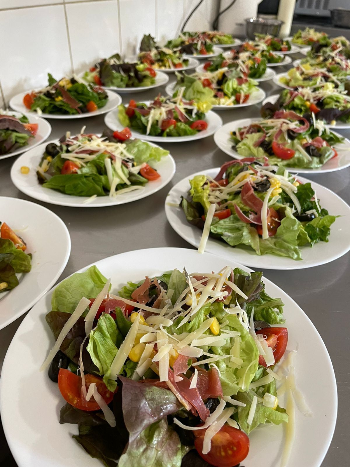 A table with multiple plates of salads, each containing various greens, tomatoes, and cheese.