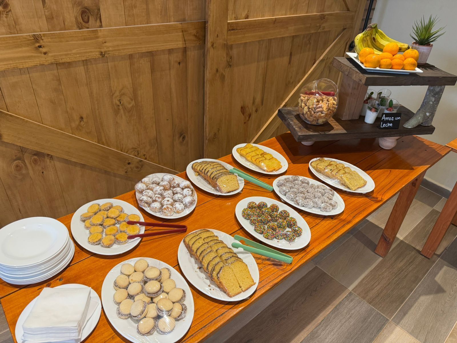 Una mesa de buffet con diversos postres y aperitivos, como galletas, pasteles y una presentación de frutas.