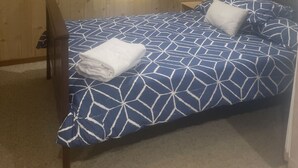 A bedroom with a bed, a nightstand, and a window with curtains. - Quaint River Shack (Caloote)