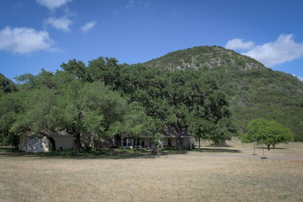 A rural property with a large open field, several trees, and a hill in the background.