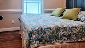 A bedroom with a bed, a ceiling fan, a window, and a wall-mounted TV.