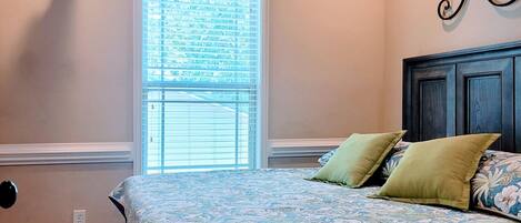 A bedroom with a bed, a ceiling fan, a window, and a wall-mounted TV.