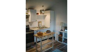 Una cocina compacta con armarios blancos, encimera de madera, lámpara colgante y una mesa pequeña con una cesta.